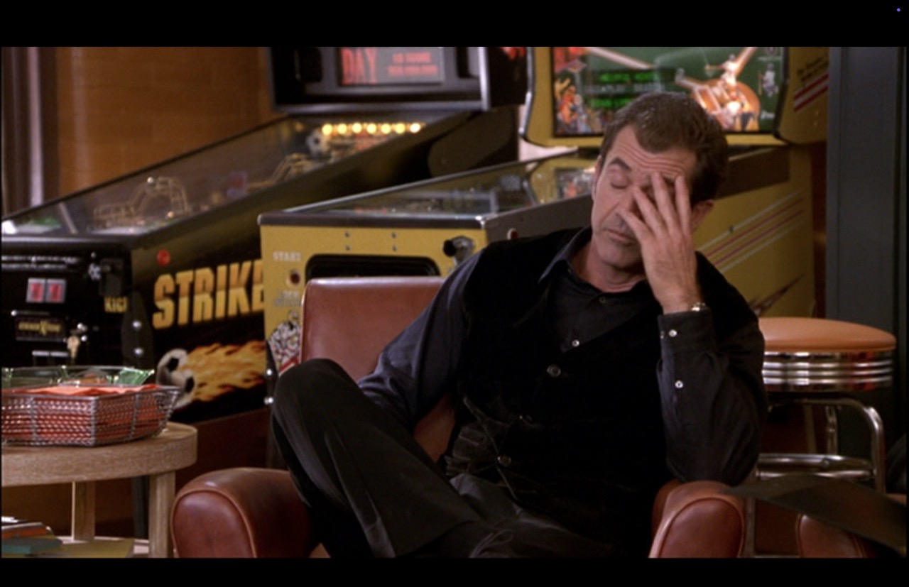 Nick reacts with dismay, his hand to his head in a medium shot. The two pinball machines dominate the background in slight non-focus. The Silver Slugger’s lights are back on.