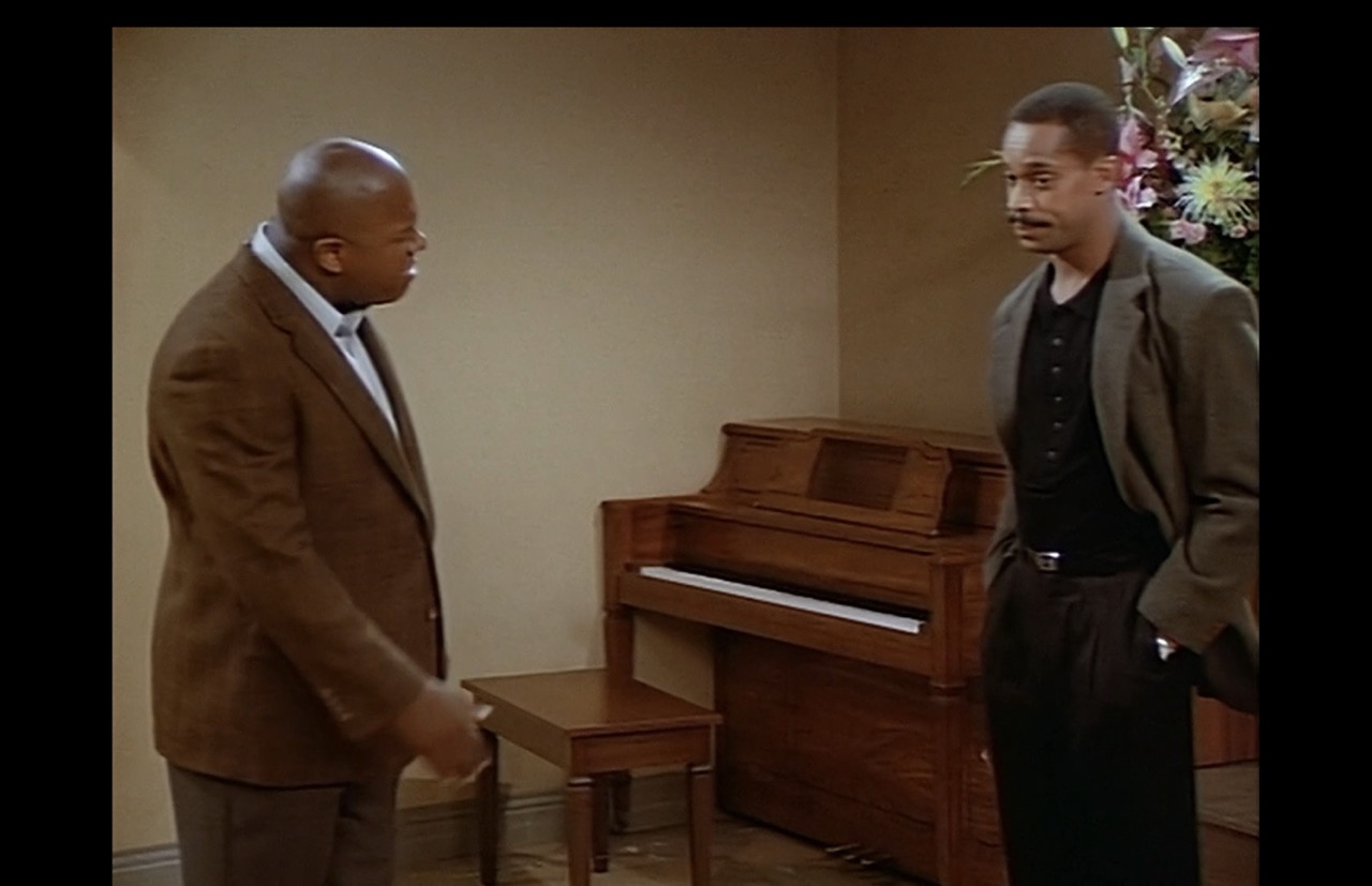 Roc has now moved toward the stage in his confrontation with Joey. The poster is no longer in frame. The background between Roc and Joey is the upright piano in a corner formed by blank walls. 